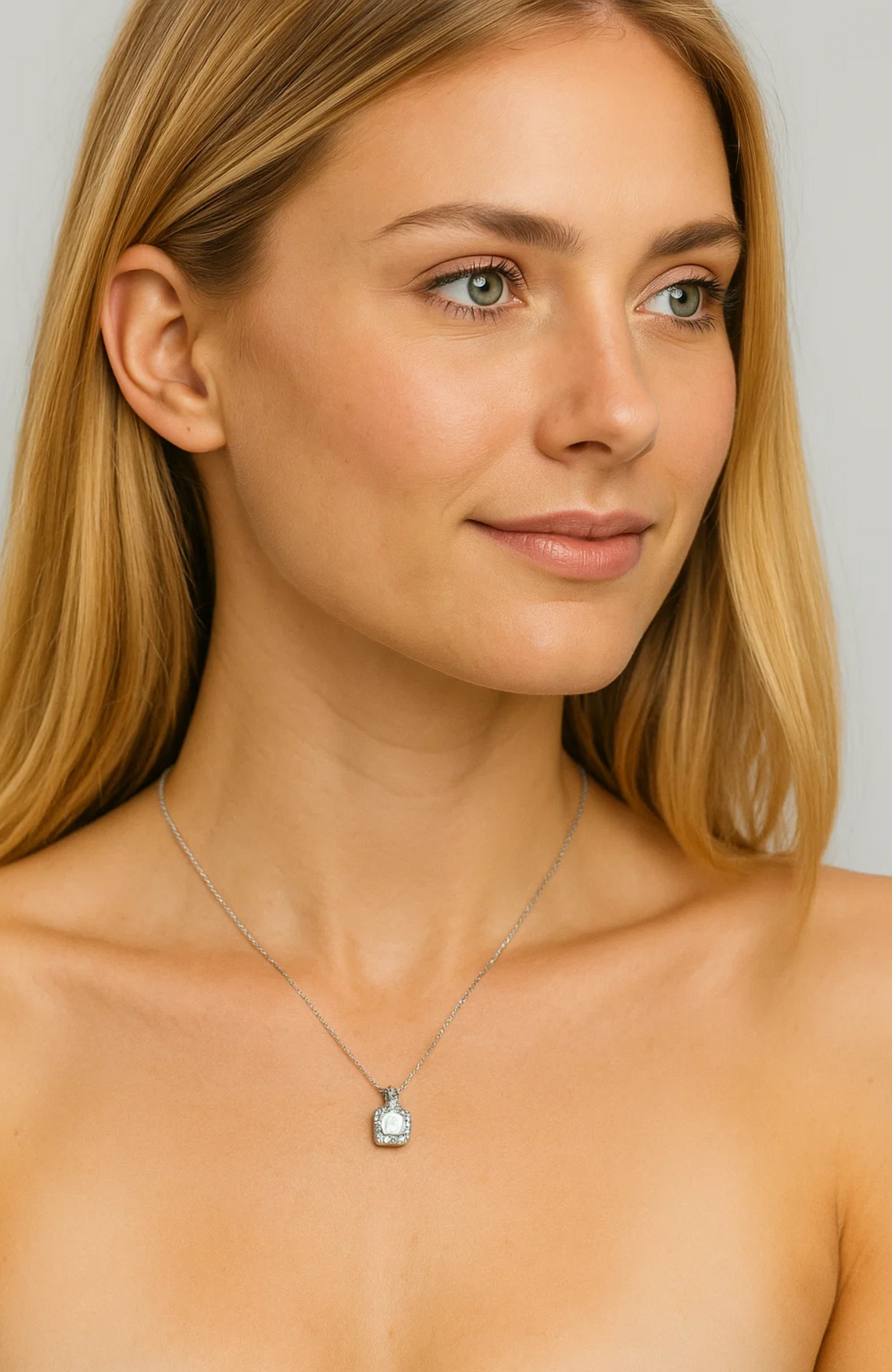 A woman with long blonde hair and a subtle smile wears the Two Carat Halo Cubic Zirconia Pendant Necklace, featuring a square-shaped pendant, while facing slightly to the side against a neutral background.