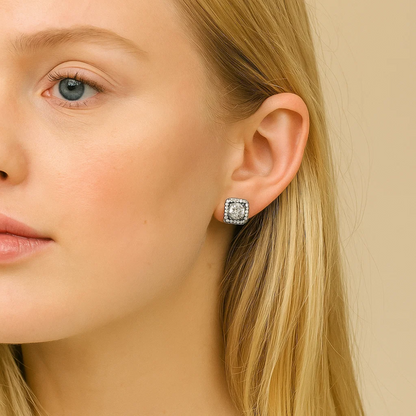 A close-up of a woman with long blonde hair wearing Katlyn Crystal Stud Earrings—square-shaped, white gold plated studs with a sparkling central stone and smaller accents—against a neutral background.