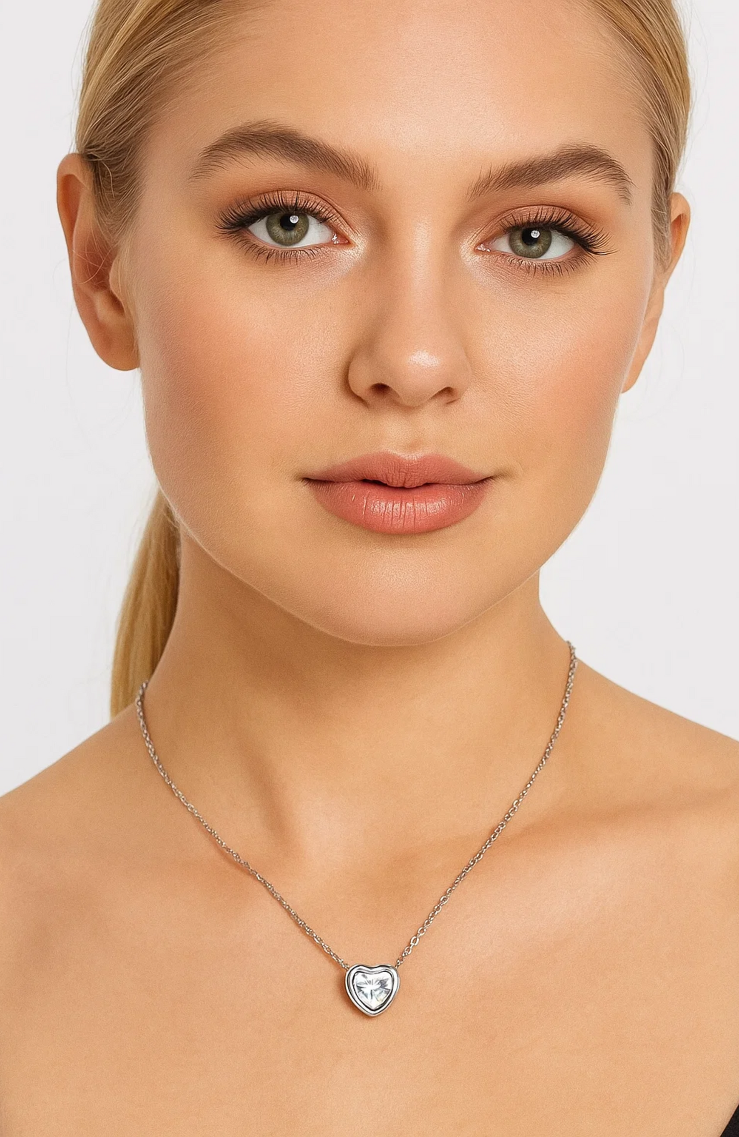 A woman with blonde hair and natural makeup wears the Heart Necklace Cubic Zirconia Crystal on a delicate white gold plated chain, set against a plain light background.