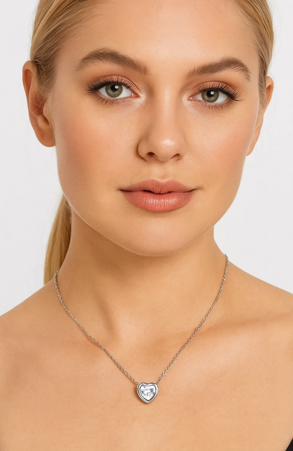 A woman with blonde hair and natural makeup wears the Heart Necklace Cubic Zirconia Crystal on a delicate white gold plated chain, set against a plain light background.