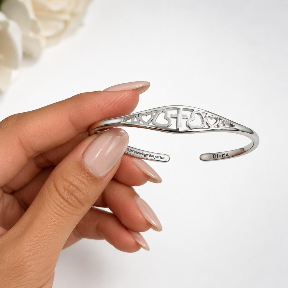 Silver adjustable cuff bracelet held in hand showing cross-and-heart cutout band
