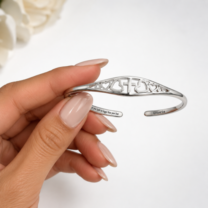 Silver adjustable cuff bracelet held in hand showing cross-and-heart cutout band