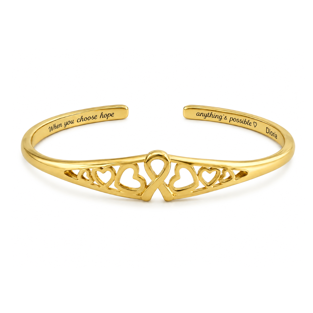 Gold engraved adjustable cuff bracelet with heart cutout ribbon motif on the front