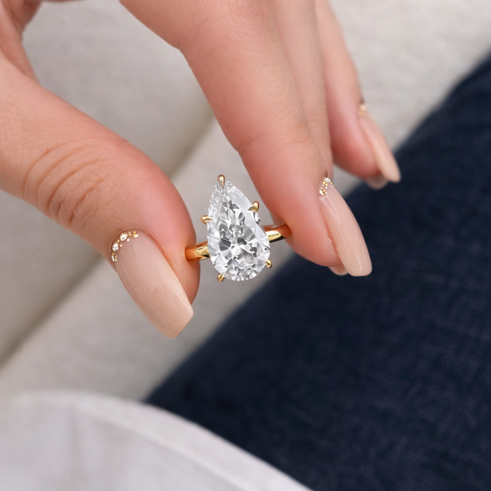 Silver-tone pear-cut moissanite ring with a teardrop center stone on finger.