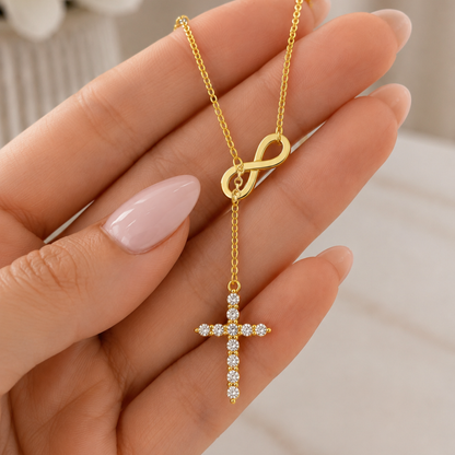 Gold lariat necklace with oval clasp and crystal cross drop, held in hand