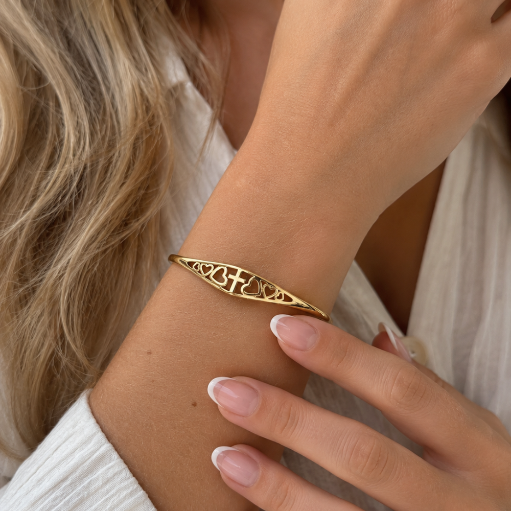 Gold cross-and-heart engraved cuff bracelet on wrist, close-up view