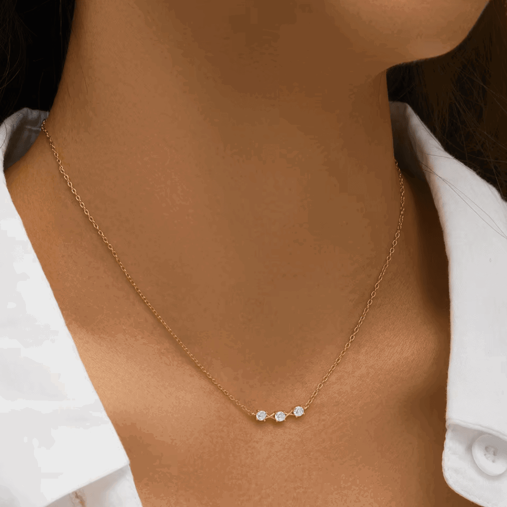 Gold-tone three-stone cubic zirconia necklace on model neckline with thin chain
