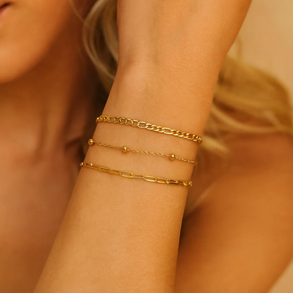Gold-tone beaded and link bracelets stacked on wrist, close-up