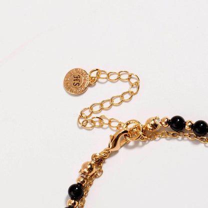 Gold beaded friendship bracelet detail with black beads and round medallion charm