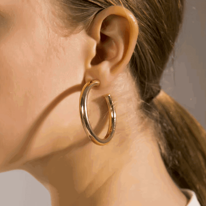 Gold-tone round hoop earrings worn on ear, larger thick hoops with pin clasp.