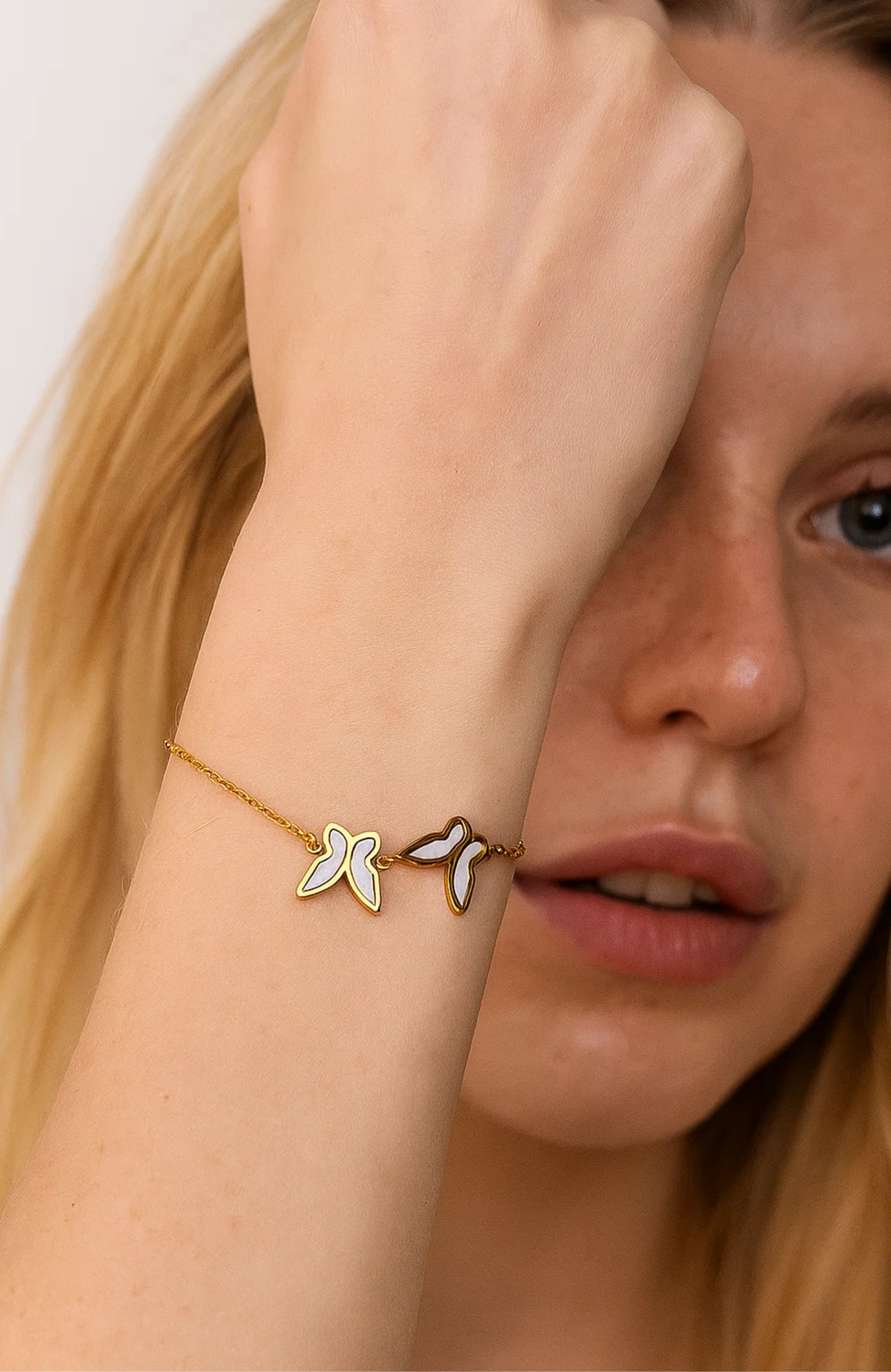 Gold bracelet with three butterfly charms and white shell inlay on wrist