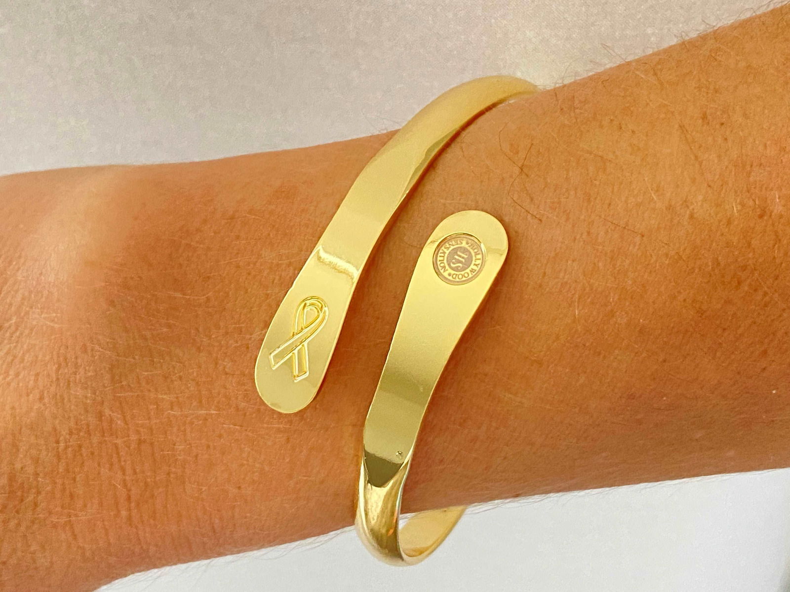 Gold cancer awareness bracelet worn on wrist, ribbon charm and round medallion