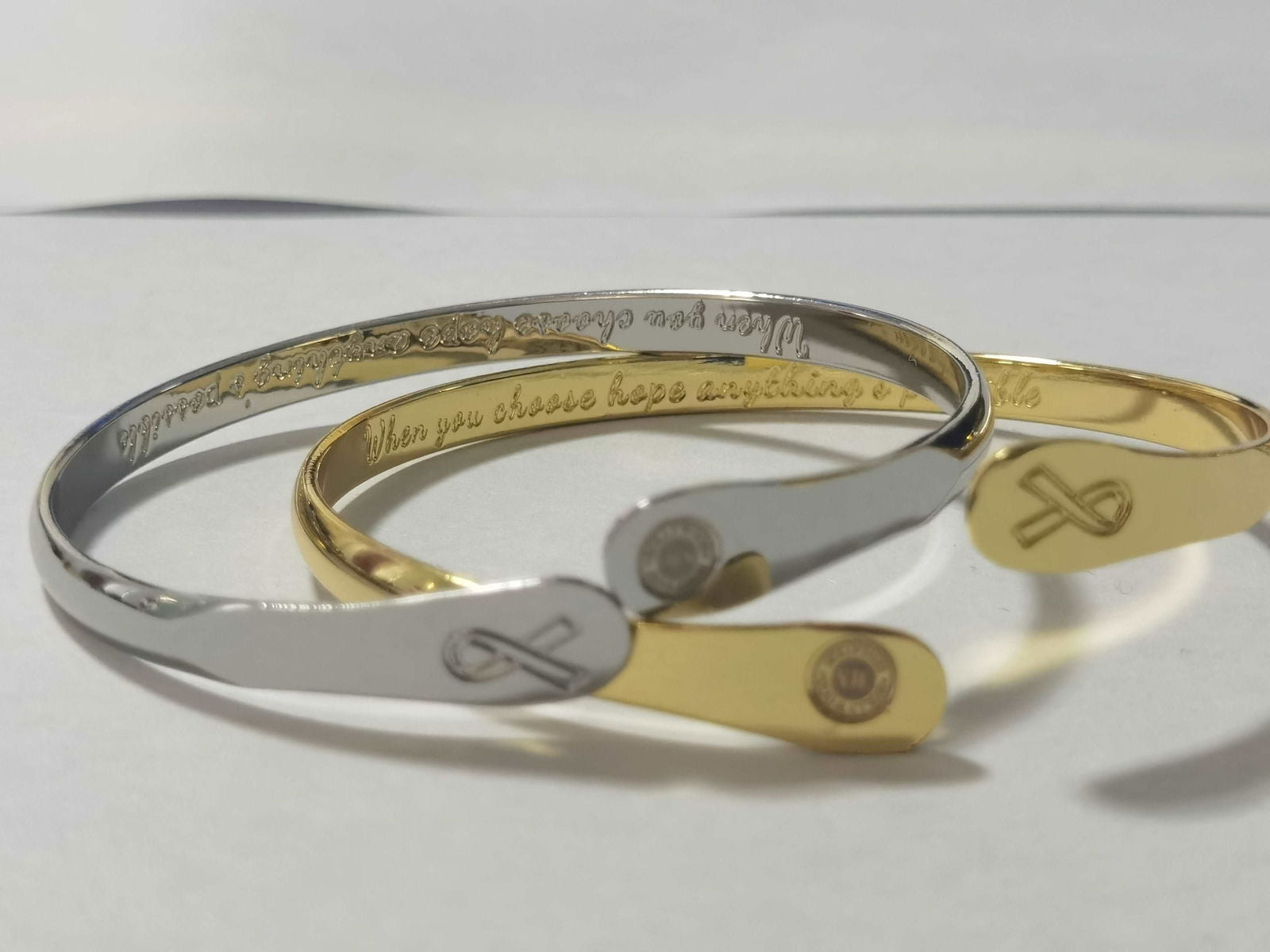 Stacked engraved bracelets, silver and gold cuffs with round logo and charm
