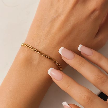 Gold chain bracelet on wrist with figaro links and manicure