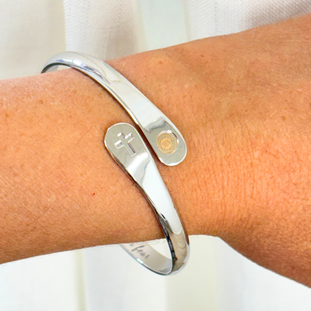 Silver cross faith bracelet cuff on wrist with cross charm and round emblem charm