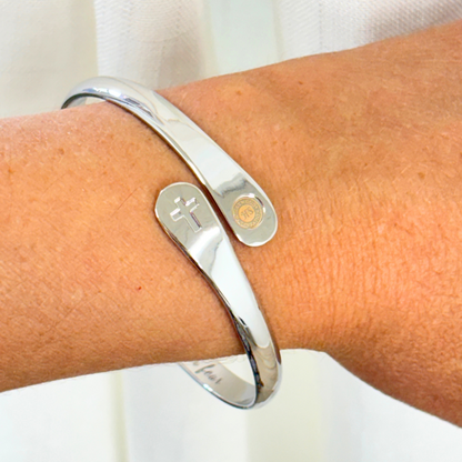 Silver cross faith bracelet cuff on wrist with cross charm and round emblem charm