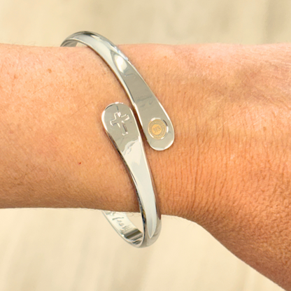 Silver bracelet cuff on wrist with cross charm and small round emblem charm
