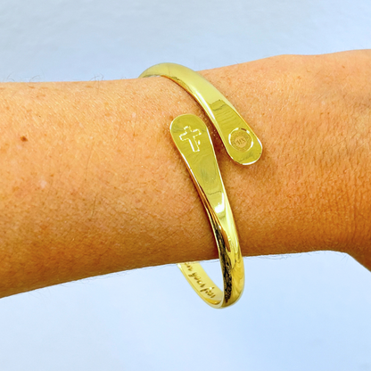 Gold cross faith bracelet cuff close-up with cross charm and round emblem charm