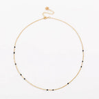Gold link necklace with black bead stations and round charm near clasp