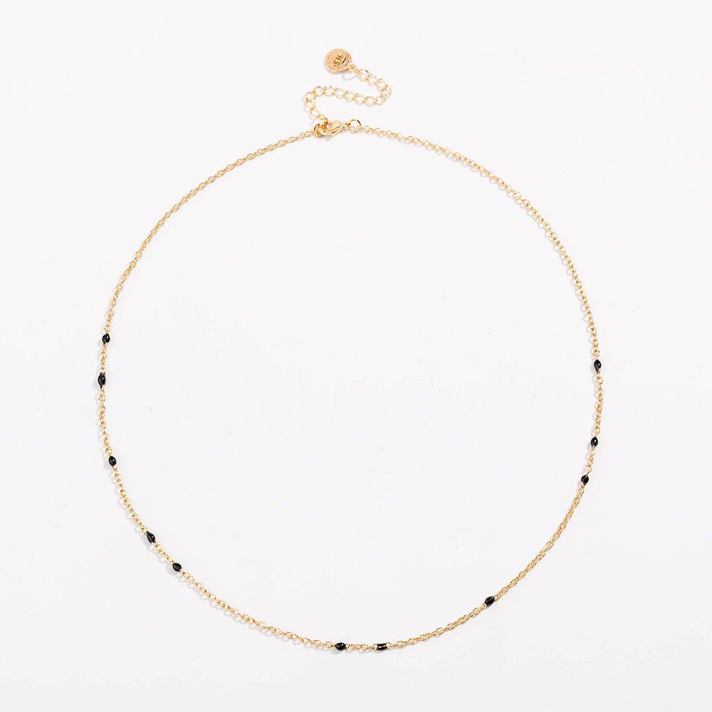 Gold link necklace with black bead stations and round charm near clasp