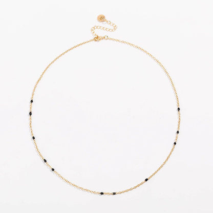 Gold link necklace with black bead stations and round charm near clasp