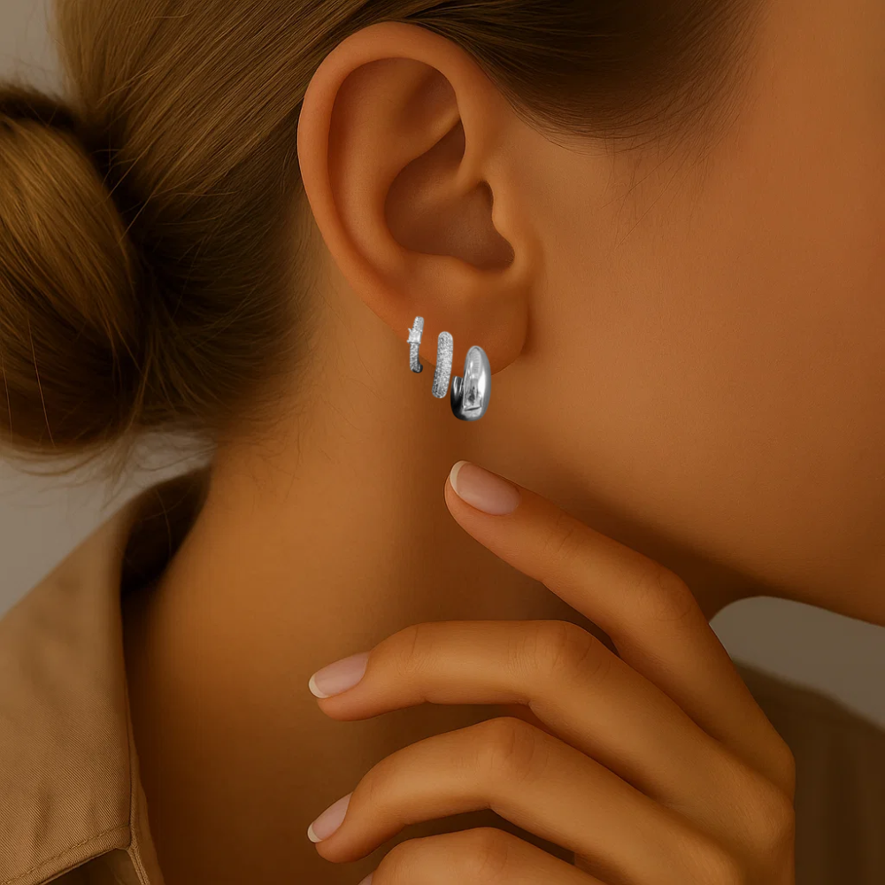 Silver-tone huggie hoop and crystal stud earrings on ear, hand near face