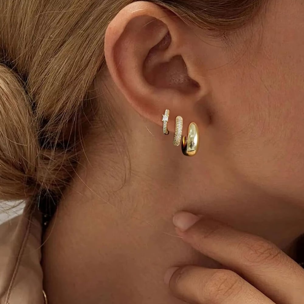 Dainty huggie hoop earrings in gold and silver, shown in one ear