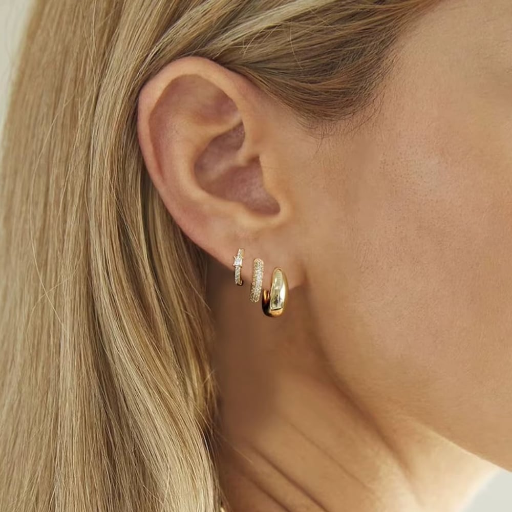 Gold huggie hoop with stones plus small hoop earrings on a side view of ear