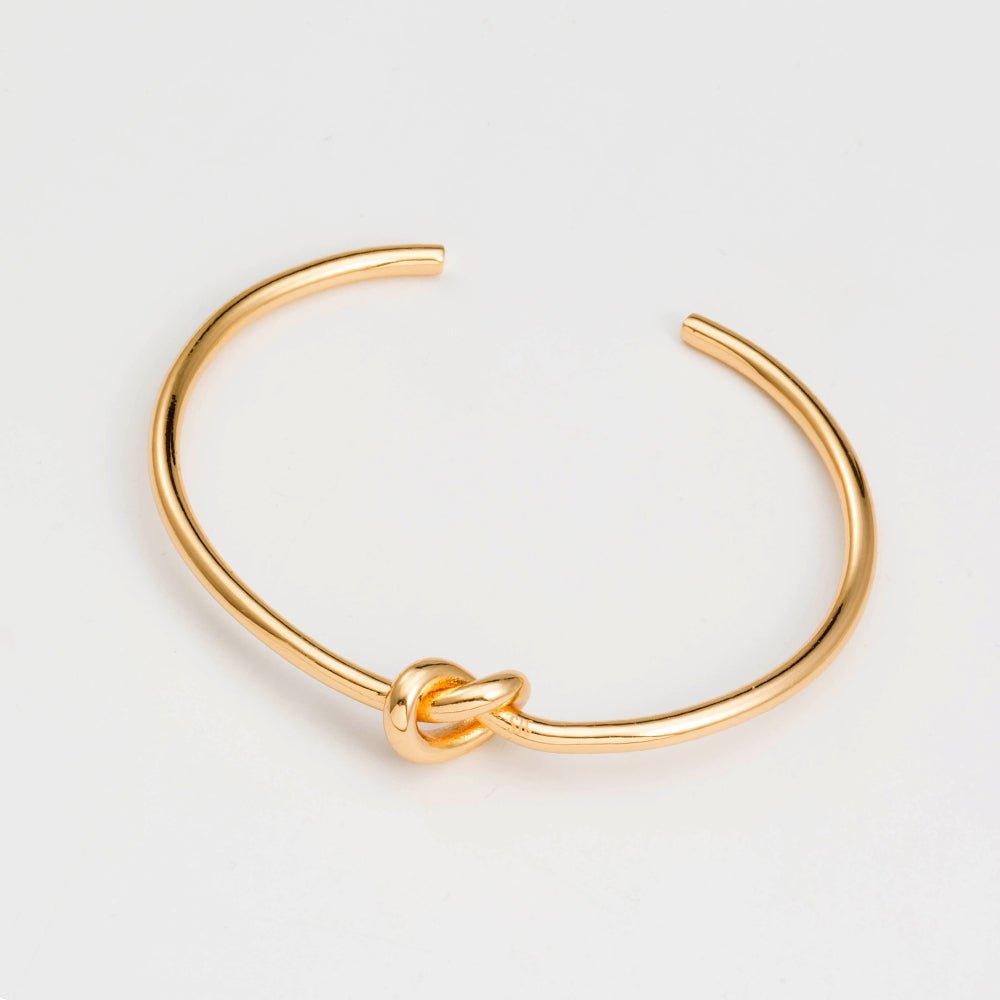 Gold love-knot bracelet featuring a twisted knot clasp on a slender bangle