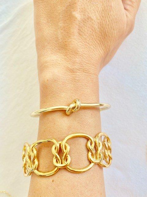 Gold love-knot bracelet on wrist with matching chain bangles