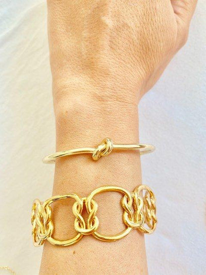 Gold love-knot bracelet on wrist with matching chain bangles