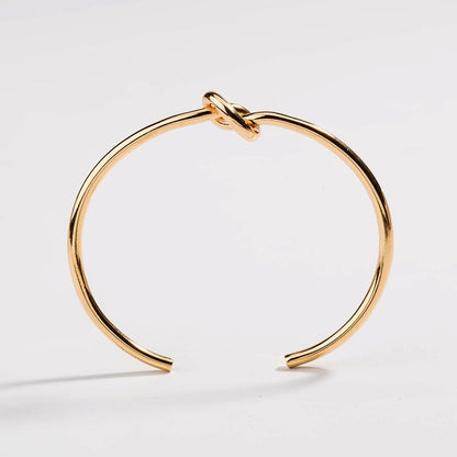 Gold love-knot bracelet with twisted knot clasp on a slender round bangle