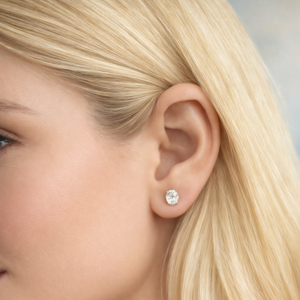 Gold oval-cut moissanite stud earrings on ear, angled side view