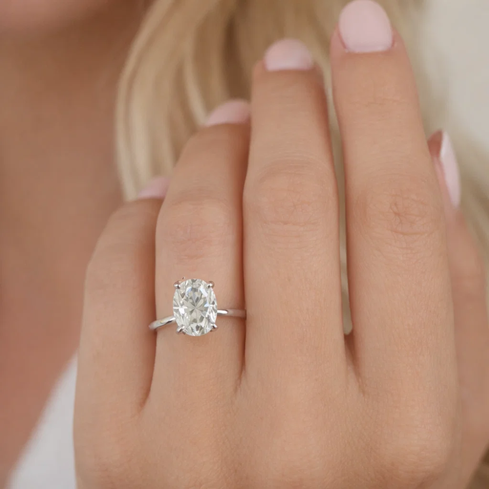 Oval cut solitaire ring on finger with silver-tone band and four-prong gemstone setting