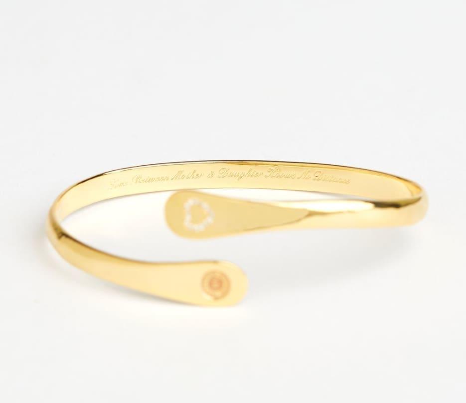 Gold engraved mother-daughter bracelet set laid flat, heart detail and round emblem