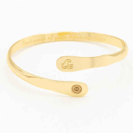 Gold wave engraved cuff bracelet with wave icon center and round side logo tag