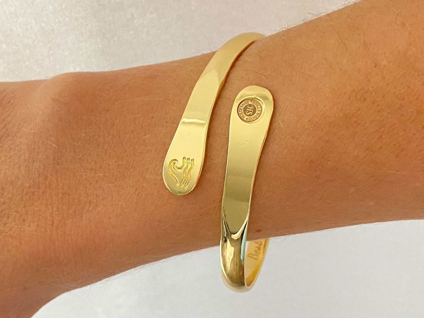 Gold wave engraved cuff bracelet on wrist with round side logo and wave motif