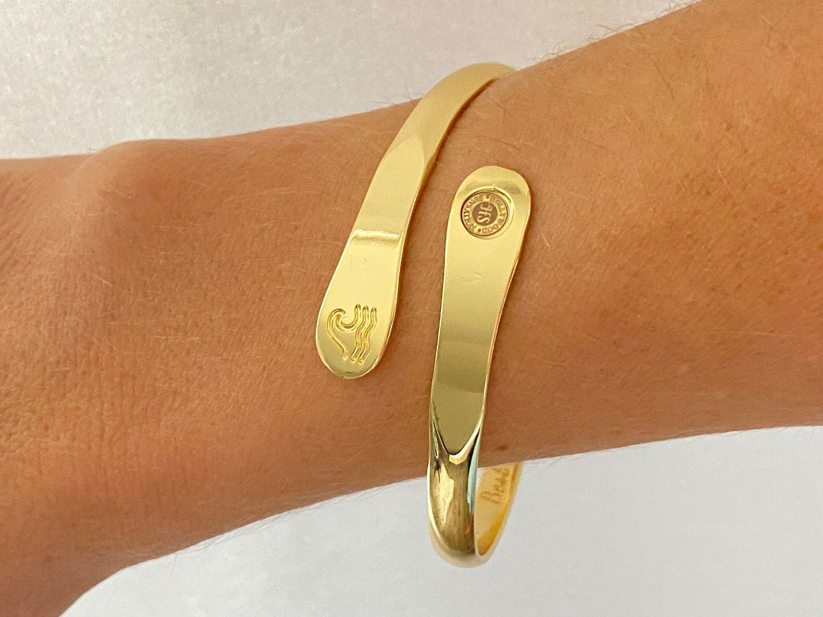 Gold wave engraved cuff bracelet on wrist with round side logo and wave motif