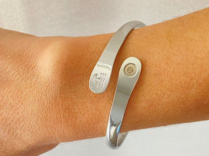 Silver wave engraved cuff bracelet on wrist with round side logo and wave motif