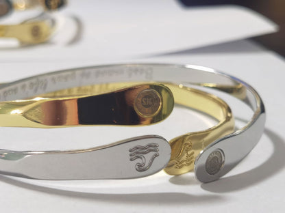 Close-up of silver and gold wave-engraved cuff bracelets with wave emblems and logo discs.