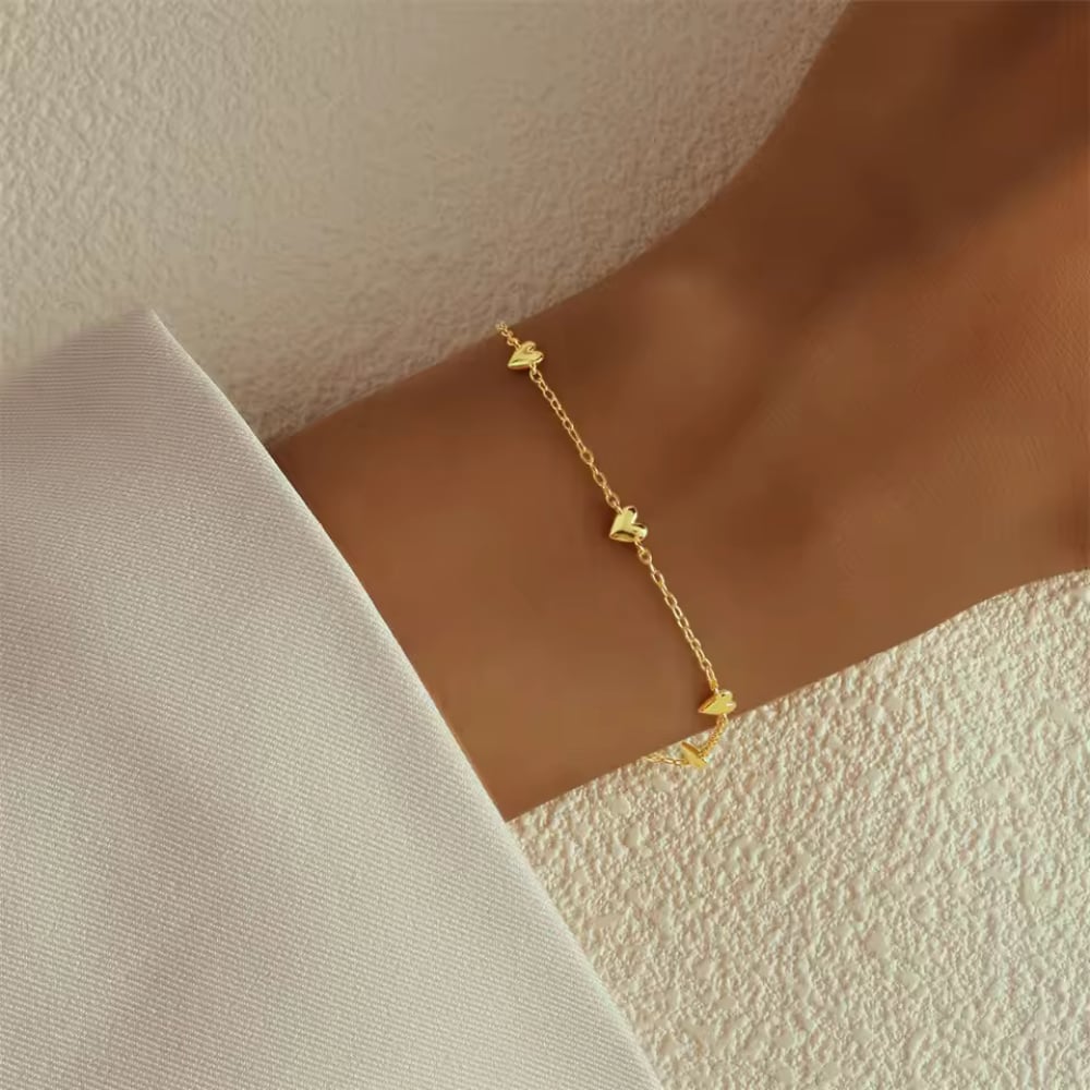 Gold heart charm bracelet on wrist with evenly spaced small heart charms