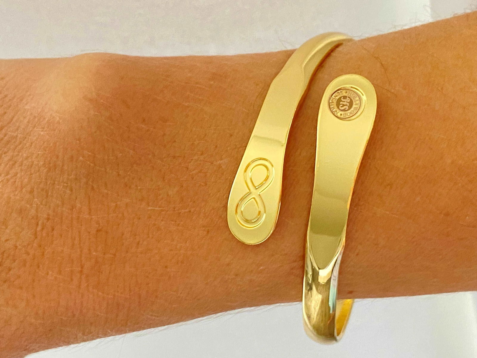 Gold infinity friendship bracelet on wrist, engraved infinity symbol and round logo charm.