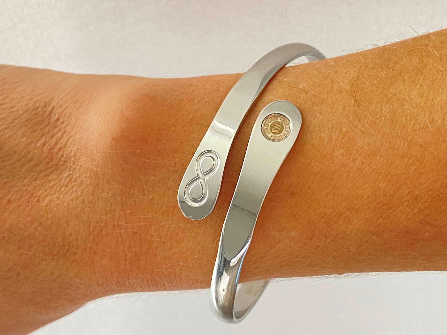 Silver infinity friendship bracelet on wrist, engraved infinity symbol and round logo charm.