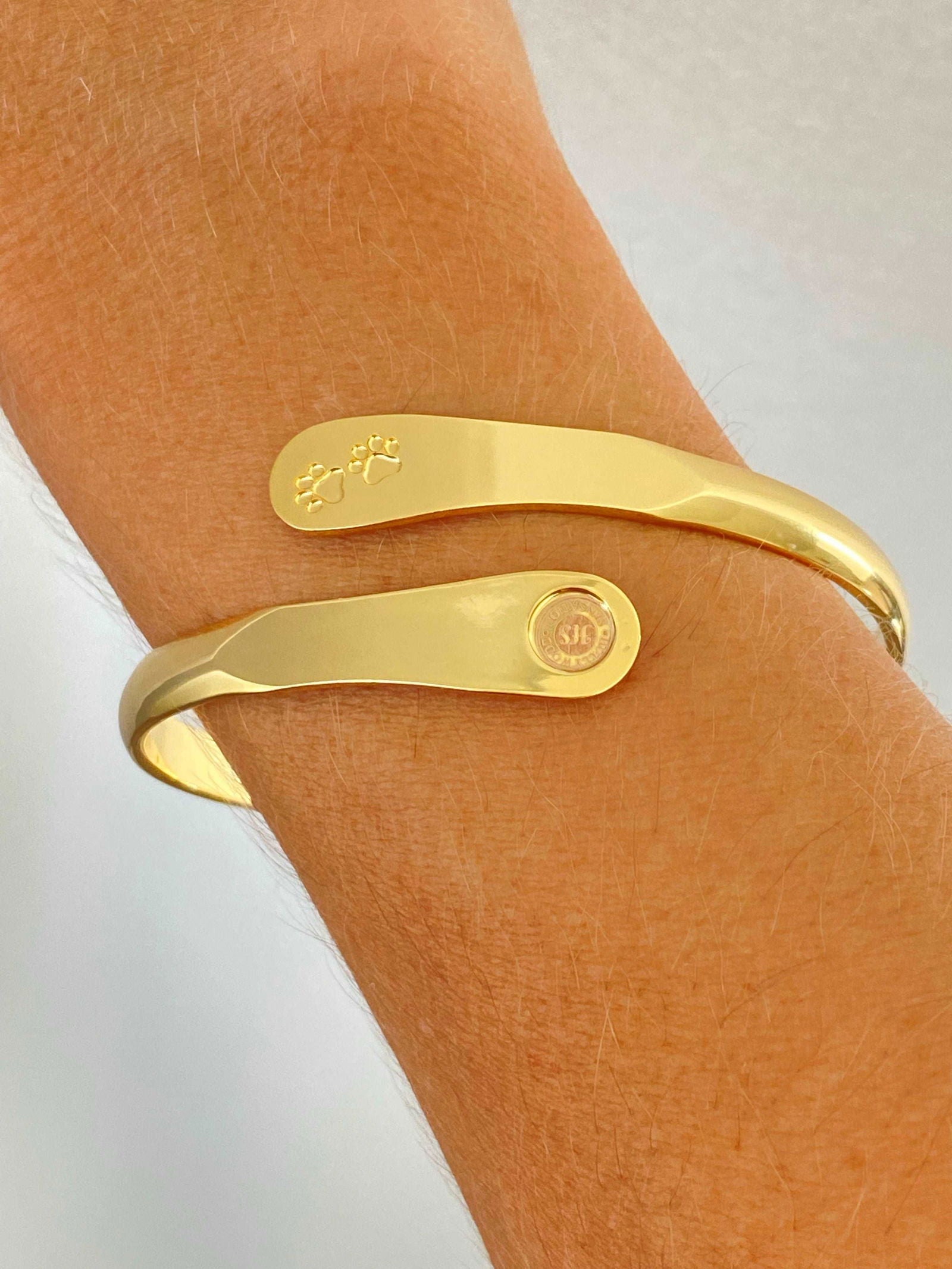 Gold paw print cuff bracelet worn on wrist with logo medallion center