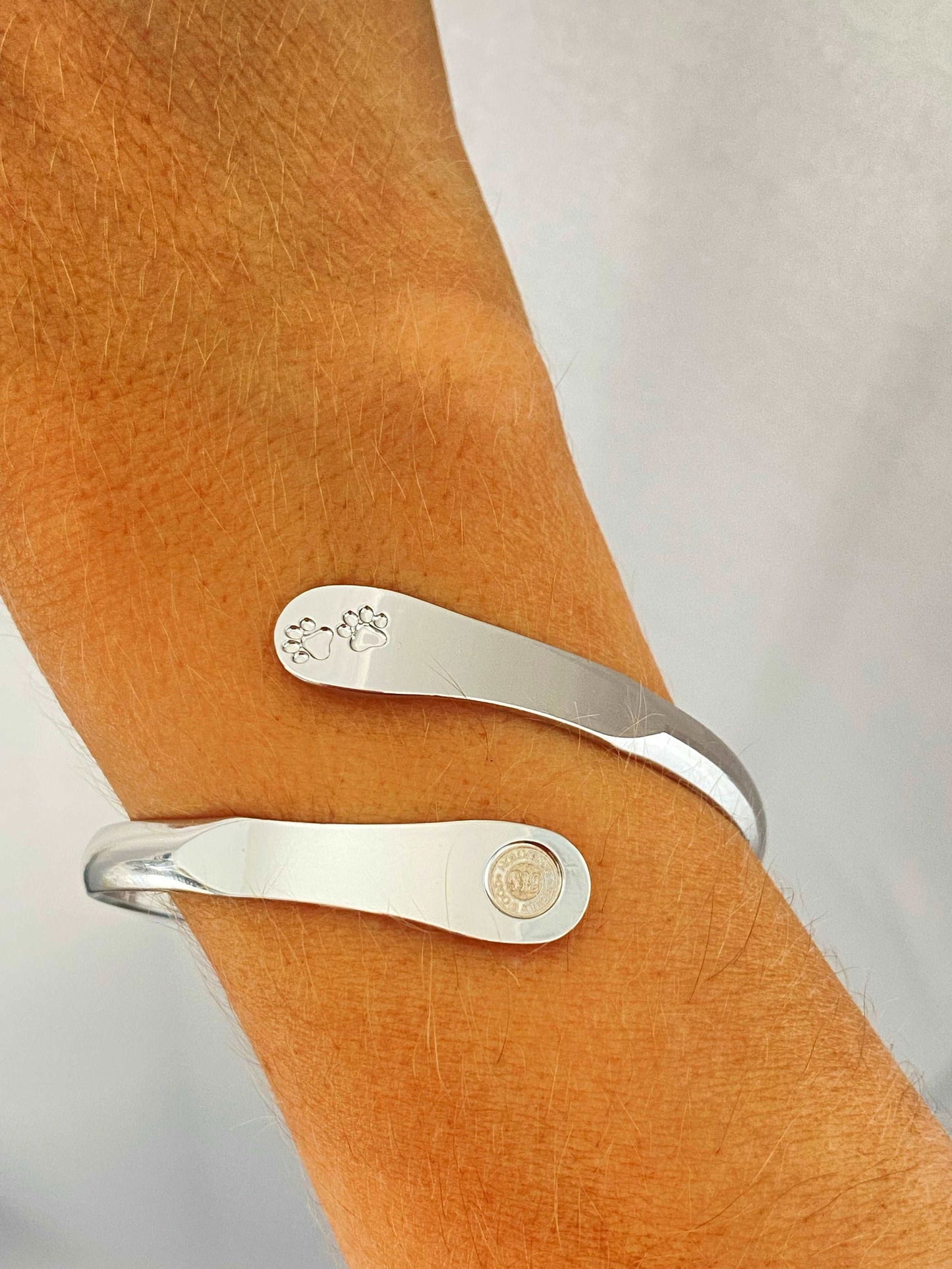 Silver paw print cuff bracelet on wrist with round logo medallion