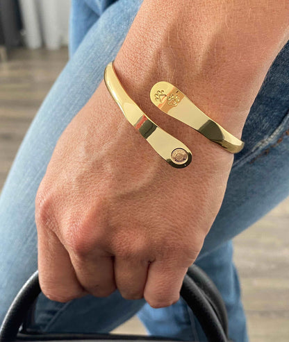 Gold paw print cuff bracelet on wrist with round logo medallion