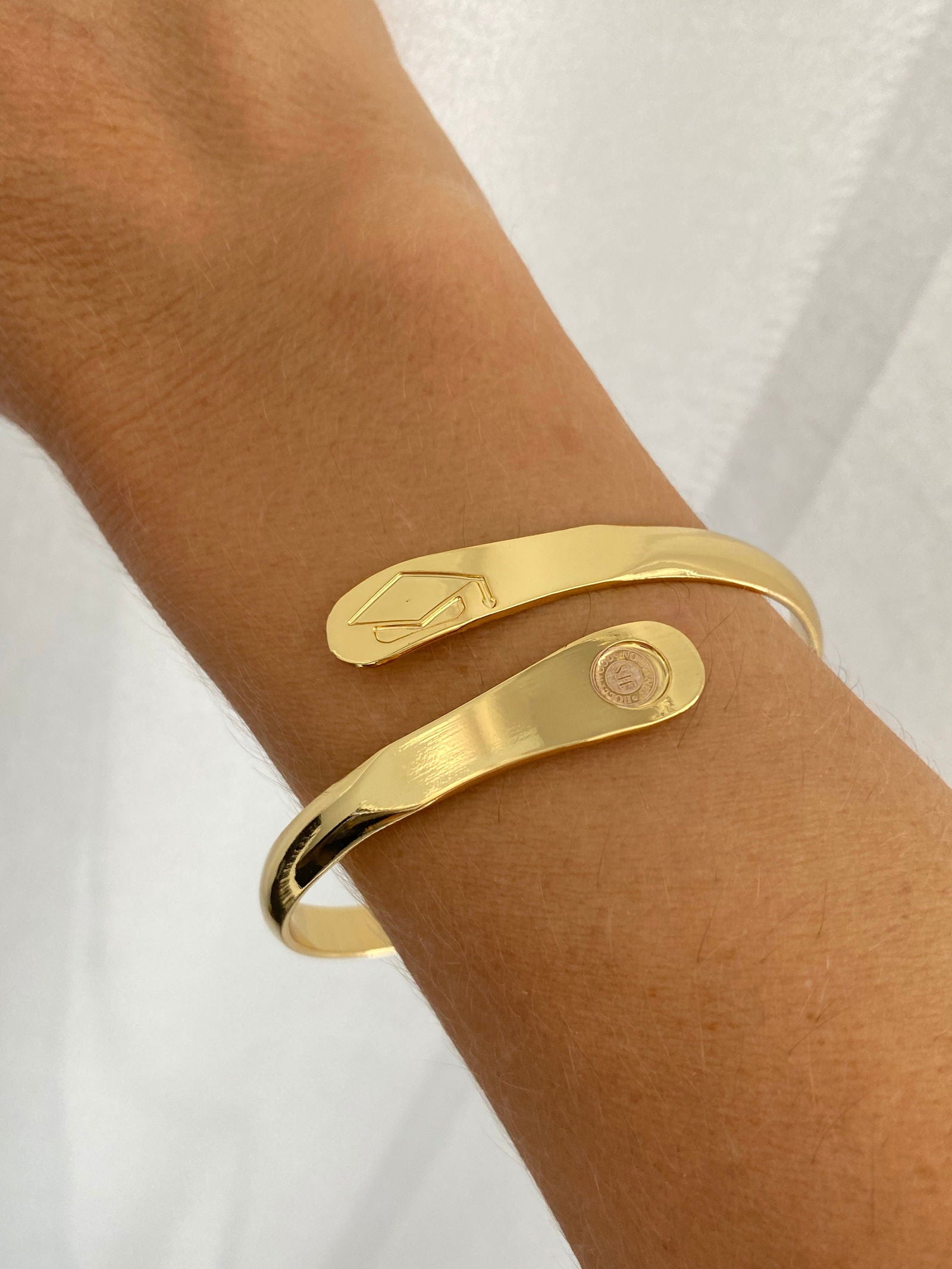 Gold graduation charm bracelet worn on wrist with cap detail and round tag