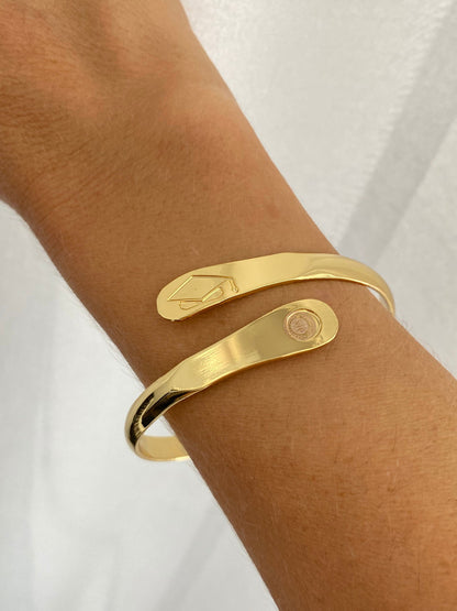 Gold graduation charm bracelet worn on wrist with cap detail and round tag