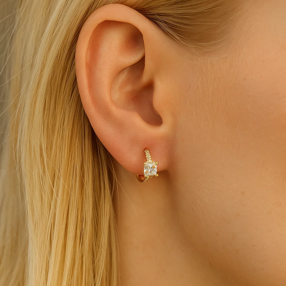 Gold square-cut huggie hoop earrings on ear with small clear stone