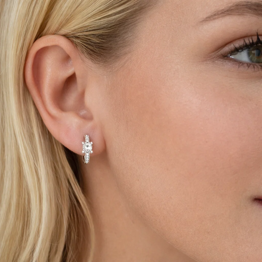 Silver square-cut huggie hoop earrings close to ear with clear center stone